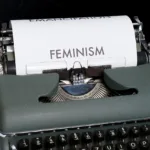 An old manual typewriter with a single page and the word FEMINISM written on it in bold letters.