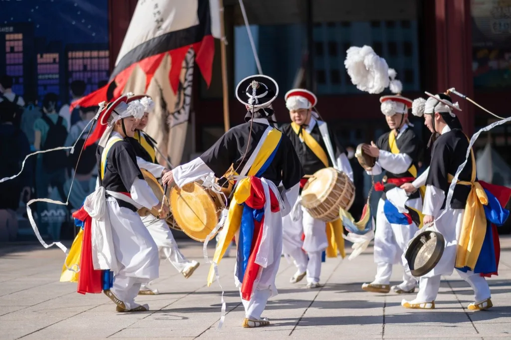 A group of Korean Samulnori ( a theater and dancing group) is dancing and playing Korean musical instruments.