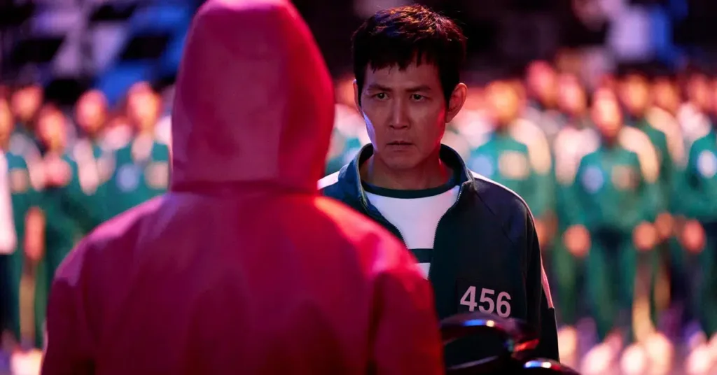 The Squid Game Gi-hun in his athletic attire with number 456 faces a man in red uniform.