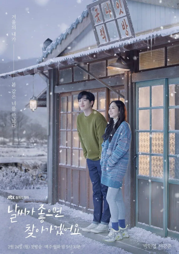Promotional poster for the JTBC Monday drama “날씨가 좋으면 찾아가겠어요” (Nalssiga Joeumyeon Chajagagesseoyo / If the Weather Is Good, I’ll Visit You). A young man in a green knit sweater and jeans stands beside a young woman in a cozy blue patterned cardigan and gray leggings, both smiling softly as they gaze into the distance under falling snow. They stand on the snowy porch of a rustic wooden house with a glowing lantern and icicles hanging from the roof. The sign above reads “굿나잇 책방” (“Goodnight Bookstore”). Korean text on the left says: “겨울의 내가 봄 같은 너를 만났다” (“In winter, I met you — who felt like spring.”). The title is written in elegant white script at the bottom, with broadcast info: “2월 24일 (월) 첫방송 매주 월화 밤 9시 30분” (First aired Feb 24, Mondays & Tuesdays at 9:30 PM). Starring Park Min-young and Seo Kang-joon. The scene evokes quiet romance, warmth, and gentle nostalgia. A poster form the best healing Korean dramas to soothe your soul.