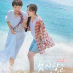 Promotional poster for the tvN Monday-Tuesday drama “첫, 사랑을 위하여” (Cheot, Sarang-eul Wihaeyeo ), streaming on TVING starting August 4. Two women — one with short hair in a white dress and colorful scarf, the other with long braided hair in denim shorts and a red plaid shirt — are joyfully running through shallow ocean waves on a sunny beach. They’re holding hands, laughing with open mouths, their clothes fluttering as water splashes around them. The background features sparkling turquoise sea under a bright blue sky. Korean text reads: “닮은 듯 다른 우리는 서로의 첫 세상, 첫 사랑이었다.” (“Though alike, we were each other’s first world, first love.”). The overall mood is warm, nostalgic, and deeply affectionate. From the list of the best healing korean dramas.