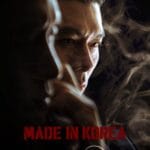 man’s face is dramatically lit from the side against a dark, smoky background, his expression intense and contemplative as he gazes off to the right. Swirling smoke or mist partially obscures his features, adding mystery and tension. His hair is slicked back, and the lighting highlights the sharp lines of his jaw and cheekbone. The title “MADE IN KOREA” is displayed in bold red capital letters across the lower portion of the image. Promotional poster for the drama Made in Korea one of the Must-Watch K-Dramas