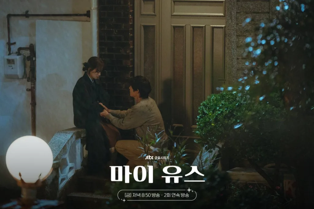 A man kneels beside a woman on stone steps at night, holding her hands under a glowing lamp. Still form My youth K-drama.