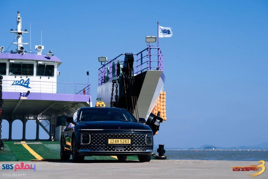 A sleek black luxury sedan is parked at the ramp of a large ferry under a clear blue sky. The car’s roof sign glows with “TAXI 모범”  and its license plate reads “서울 24마 5283.” Behind it, the white-and-purple ferry, marked “1004,” stands ready for departure, its ramp lowered onto the dock.